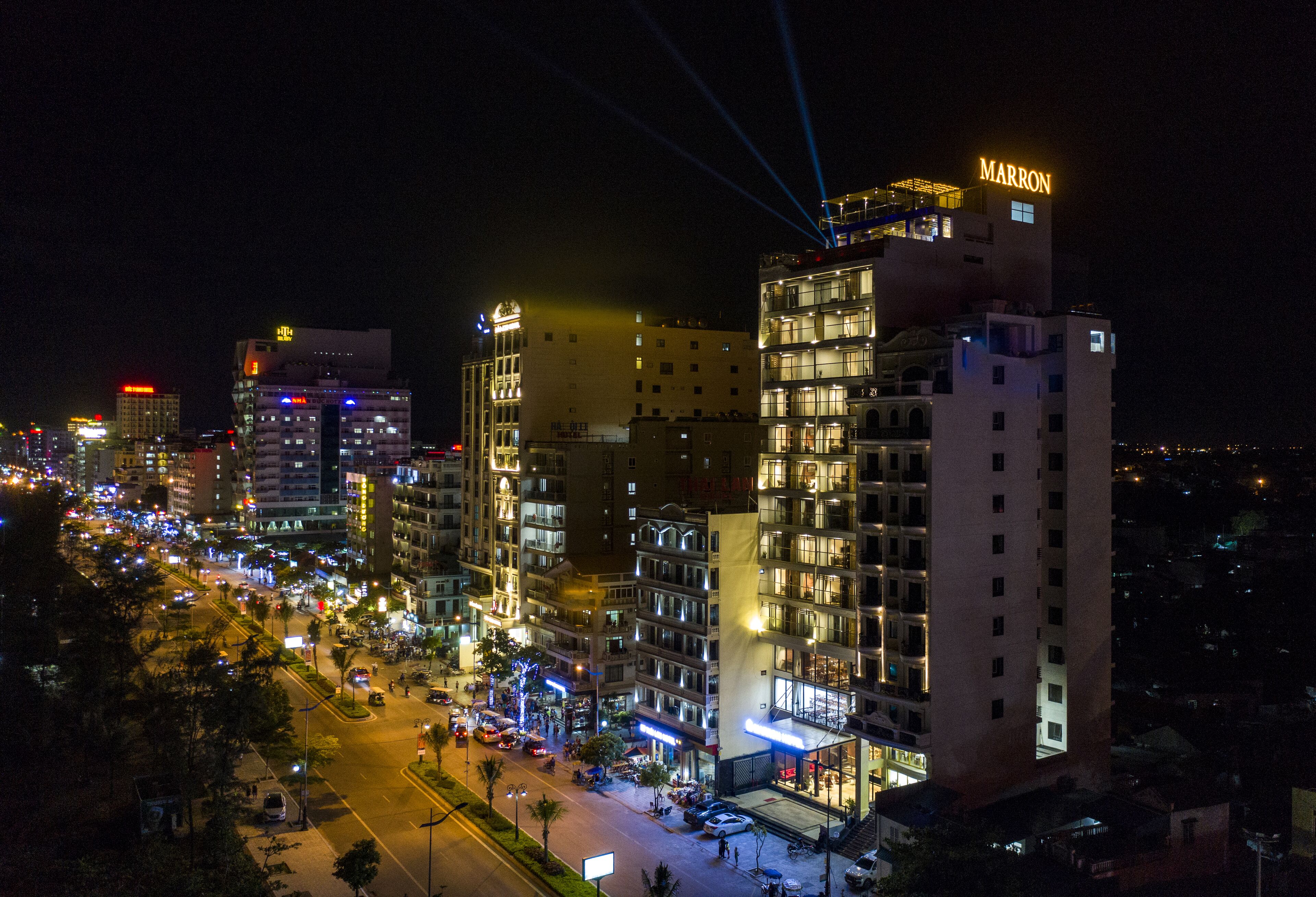 Un hôtel à plusieurs étages, doté d’une enseigne lumineuse, d’une cour intérieure et entouré d’immeubles urbains.