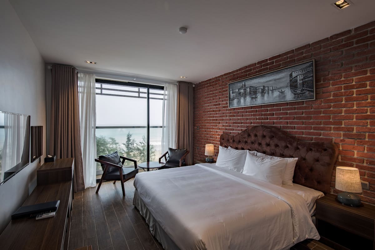 A hotel room with a large bed, a TV, a chair, and a view of the outdoors.