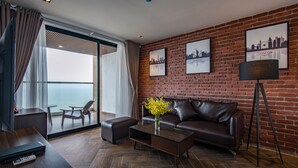 A modern living room with a leather sofa, a coffee table with a vase of flowers, a TV, and a brick wall with cityscape pictures. - The Marron Hotel (Sam Son)