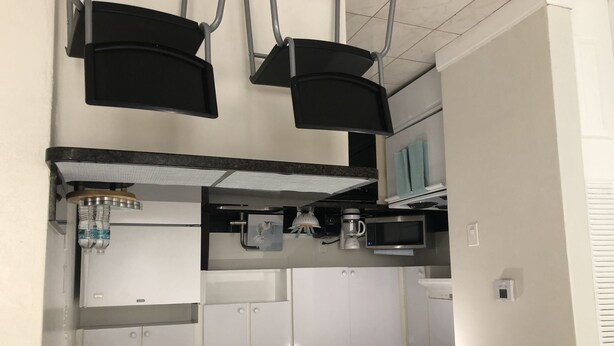 A modern kitchen with white cabinets, a microwave, a coffee maker, and a hanging light fixture.