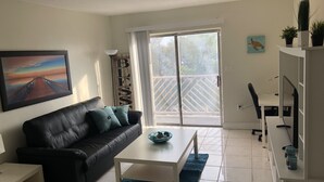 A modern living room with a black leather sofa, a white coffee table, and a painting of a sunset pier.