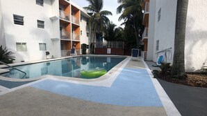 A swimming pool with a green inflatable ring, surrounded by a building with balconies and palm trees.