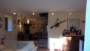A spacious living room with a fireplace, a dining area, and a kitchen with wine bottles. - Beautiful Villa in Maremma (Farnese)
