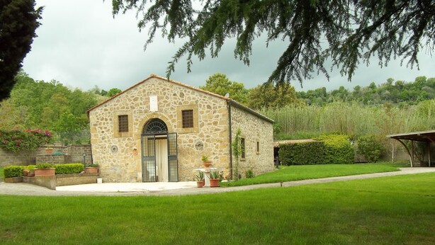 A stone building with a tiled roof, a central entrance, and a small garden area with potted plants. - Beautiful Villa in Maremma (Farnese)