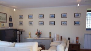 A living room with a white sofa, a coffee table, and a TV. There are framed pictures on the wall and a window with blinds. - Beautiful Villa in Maremma (Farnese)