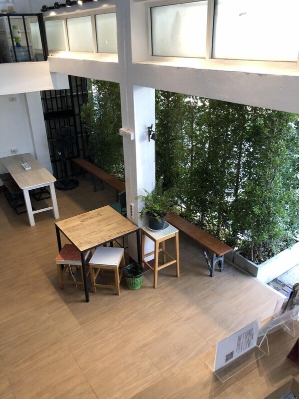 An indoor space with a wooden table and benches, surrounded by large windows and greenery. - Ploy Hostel (Bangkok)