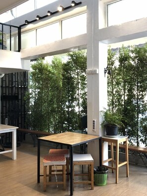 Un interior moderno con una mesa y sillas de madera, ventanas amplias y plantas de interior.
