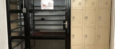 A security door with a notice sign, a mesh screen door, and a set of beige lockers with numbered doors.