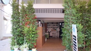L’entrée d’un hôtel, avec un banc en bois, des plantes en pot et un panneau indicateur.