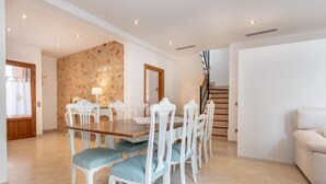 Un comedor con una mesa de madera y sillas blancas, una escalera y un sofá color beige.