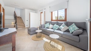 Un amplio espacio habitable con un sofá gris, dos mesitas redondas, una mesa de centro de madera y una escalera que lleva a un piso superior.