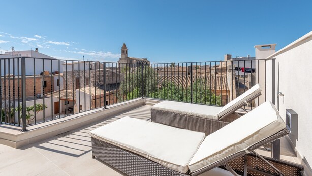 Terraza en la azotea con vistas a edificios, una baranda y dos sillones de descanso.