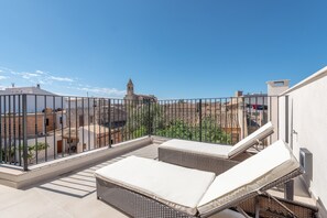 A rooftop terrace with a view of buildings, a railing, and two lounge chairs.