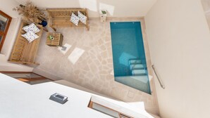 Zona de piscina en la azotea con suelo de piedra, mobiliario de madera y vistas a la piscina.