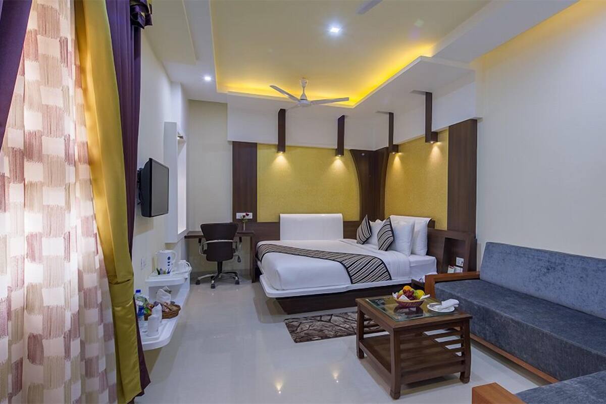 A hotel room with a bed, a sofa, a desk, a TV, and a ceiling fan.