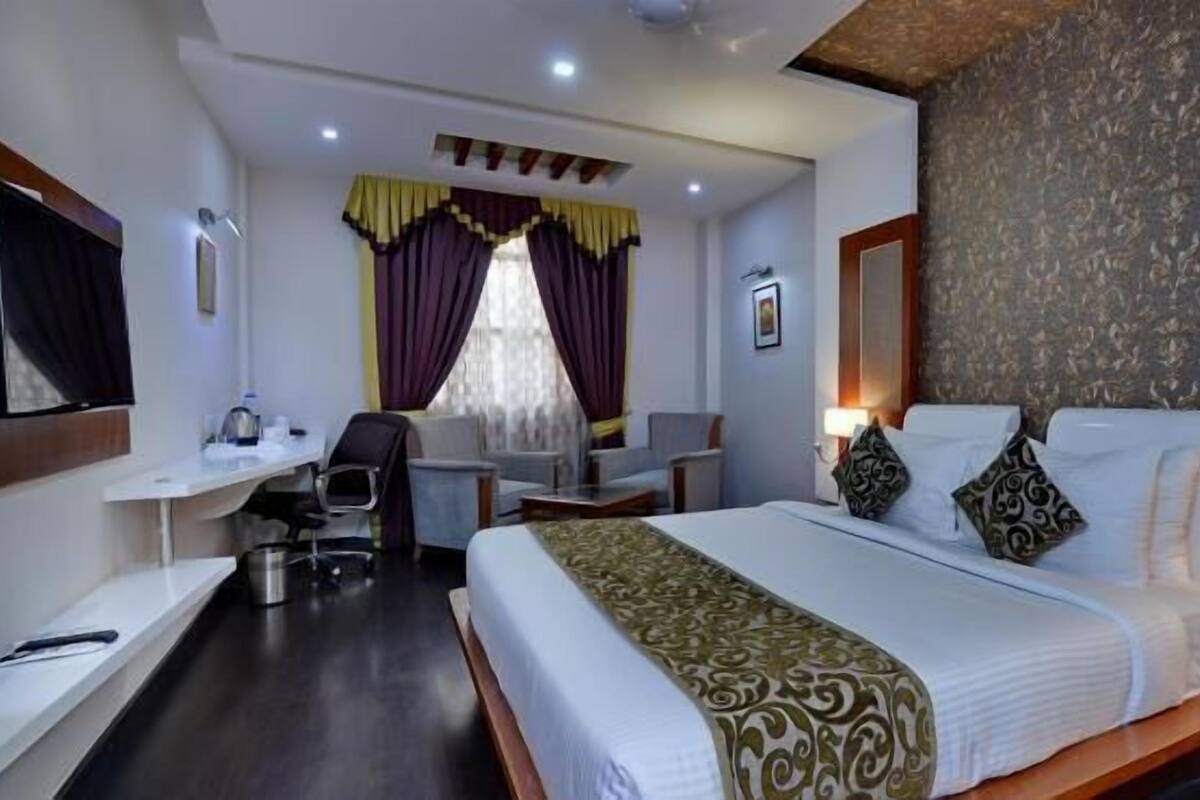 A hotel room with a large bed, a desk, a chair, and a small table.
