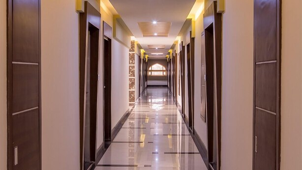 Un largo y estrecho pasillo de hotel con puertas a ambos lados, suelo pulido e iluminación empotrada en el techo.