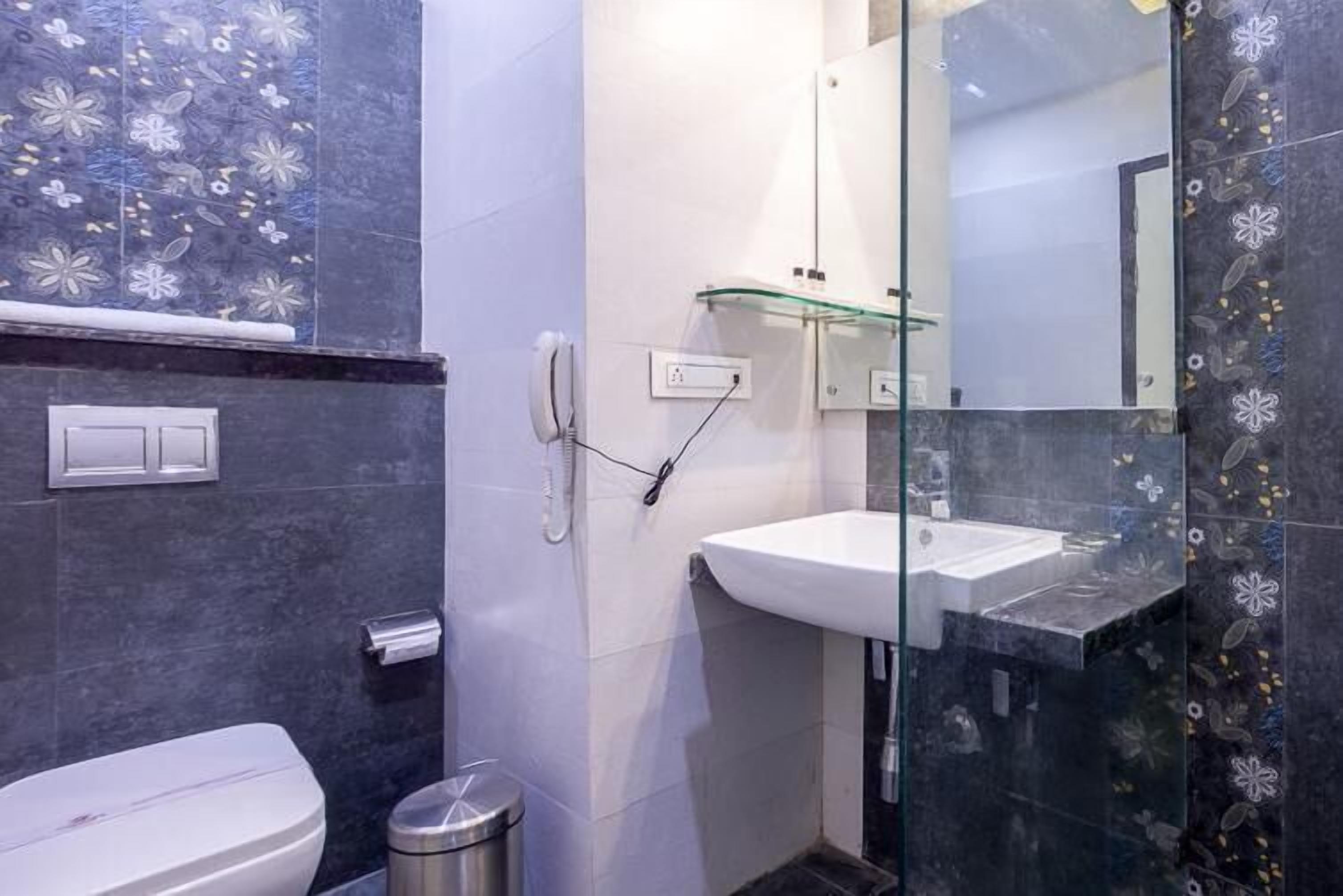 Un bany amb un vàter, un box de dutxa de vidre i un lavabo amb una prestatgeria de vidre a sobre.