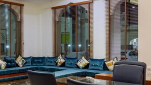 Una sala moderna con un sofá seccional azul, persianas de madera y una mesa de centro de vidrio.