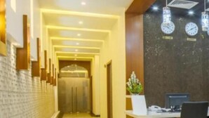 Un área de recepción de hotel con diseño moderno, que incluye un mostrador de recepción, una computadora y una zona de estar.