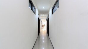 Un pasillo largo y estrecho con paredes blancas y un piso brillante, que conduce a una habitación luminosa al final.