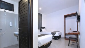 Habitación de hotel con cama, escritorio, silla, televisor y baño con lavamanos y ducha.