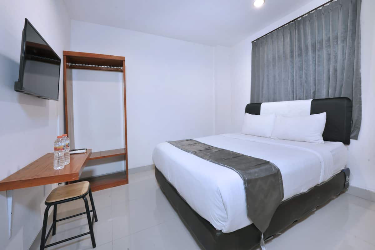 Habitación de hotel con cama, escritorio con silla, televisor montado en la pared y ventana con cortinas.
