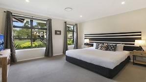A modern hotel room with a large bed, a desk with a computer, and a view of a garden through the windows. - 1OAK - THE VINTAGE HOLIDAY HOUSES (POKOLBIN)