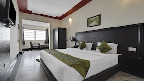 Habitación de hotel con una cama grande, un televisor montado en la pared, un escritorio con una silla y una ventana con persianas.