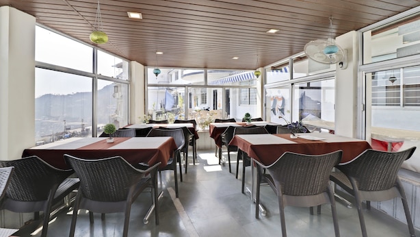 Un restaurante con techos altos, amplias ventanas y sillas de mimbre. Las mesas están dispuestas con manteles marrones y centros de mesa.