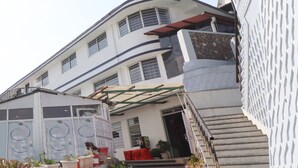 Un edificio de varios pisos con un balcón, un área exterior cubierta con plantas y una escalera que conduce a la entrada.