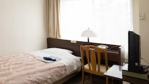 Habitación de hotel con una cama individual, una silla de madera, un escritorio con una computadora y una ventana con cortinas.