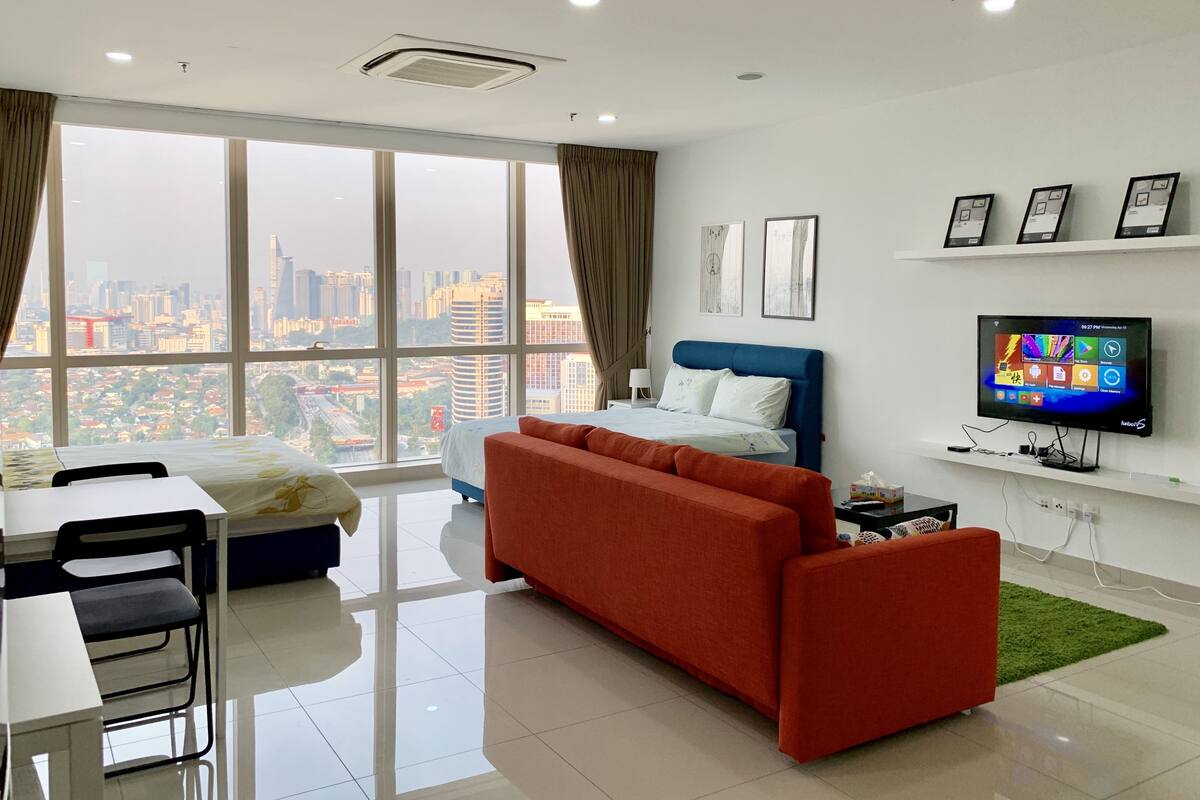 Quarto de hotel moderno com uma grande janela, uma cama, um sofá, uma televisão e uma escrivaninha.