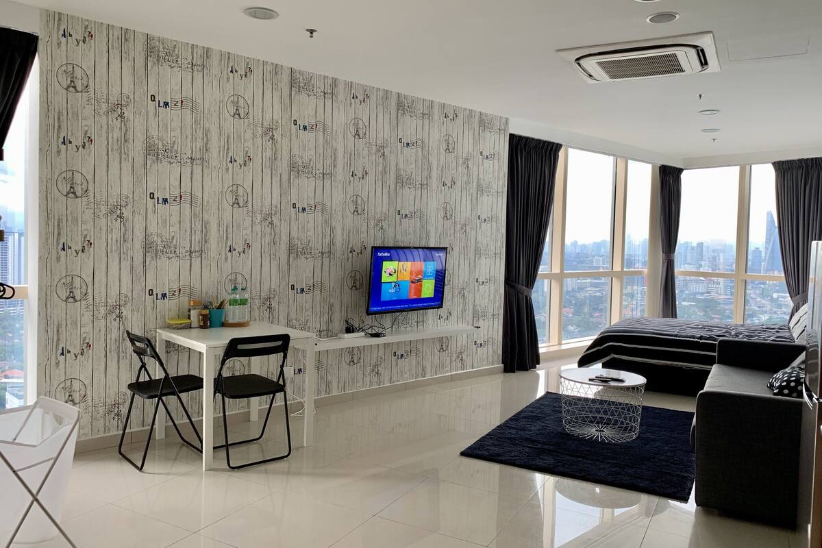 Quarto de hotel moderno com vista para a cidade, televisão de tela plana, escrivaninha com duas cadeiras e um sofá.