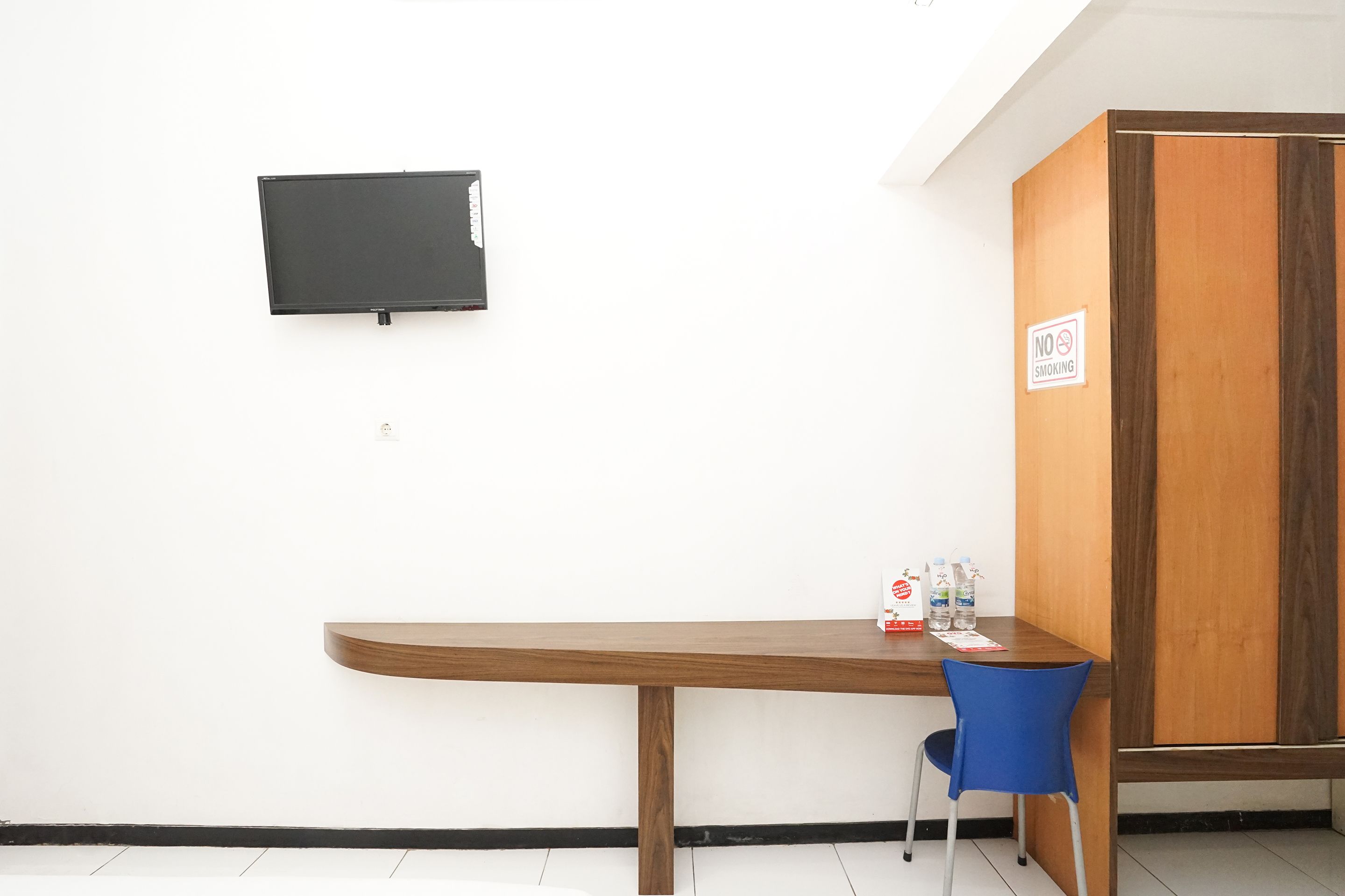A room with a wooden desk, a blue chair, a blackboard, and a wardrobe with a 'No Smoking' sign.