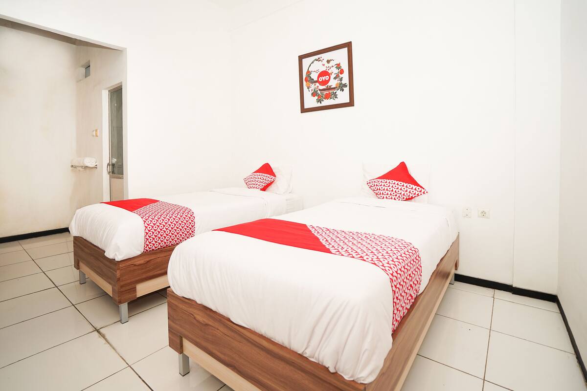 Two single beds with white and red bedding, a wooden headboard, and a small framed picture on the wall.