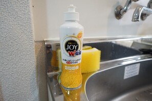 A bottle of Joy W detergent with a lemon scent, placed next to a stainless steel sink and a yellow sponge. - Apartment Camon EBR0001E (Osaka)