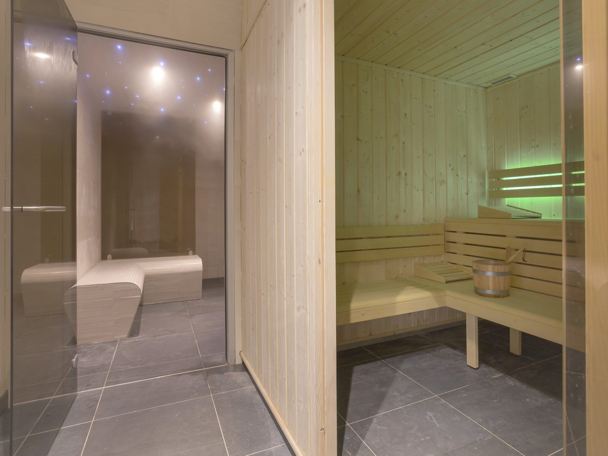 A sauna room with wooden benches and a glass door leading to a shower area.