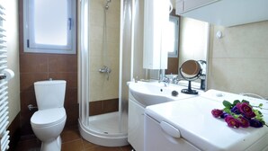 Un baño con inodoro, cabina de ducha, lavabo con espejo y un ramo de flores sobre el mostrador.