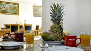 Una mesa de desayuno con platos, cubiertos, una piña, un mango y una taza de Nescafé Classic.
