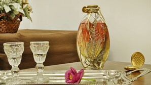 Una bandeja de plata con dos vasos de vidrio transparente, una botella de vidrio decorativa, una flor rosa.