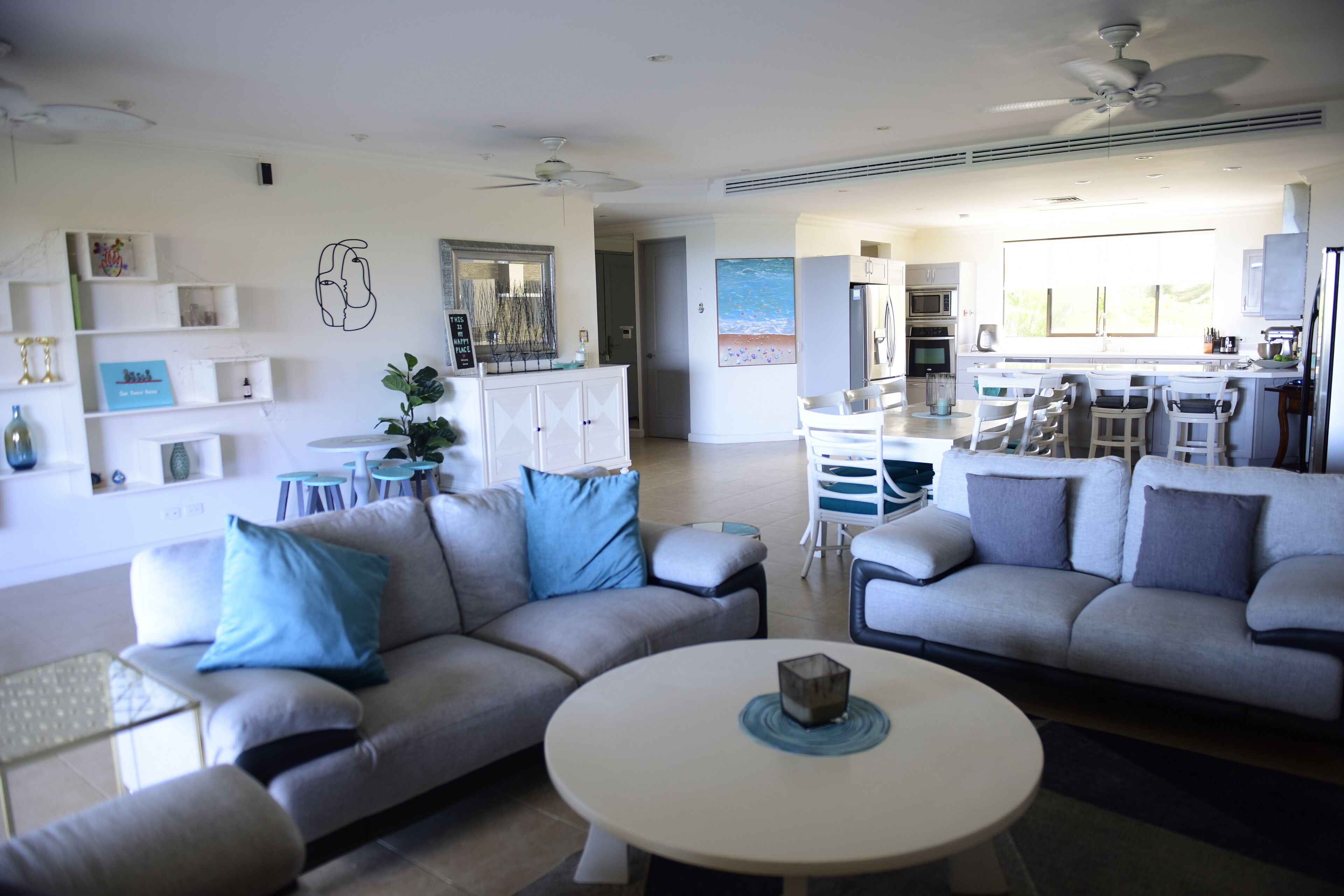 A modern living room with two grey sofas, a white coffee table, and a dining area with a bar.