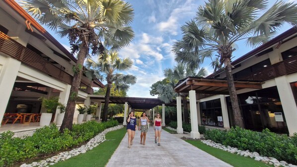 A covered walkway flanked by palm trees and a building with a modern architectural style. - Ocean View Luxury Family Condo Reserva Conchal! (Cabo Velas)