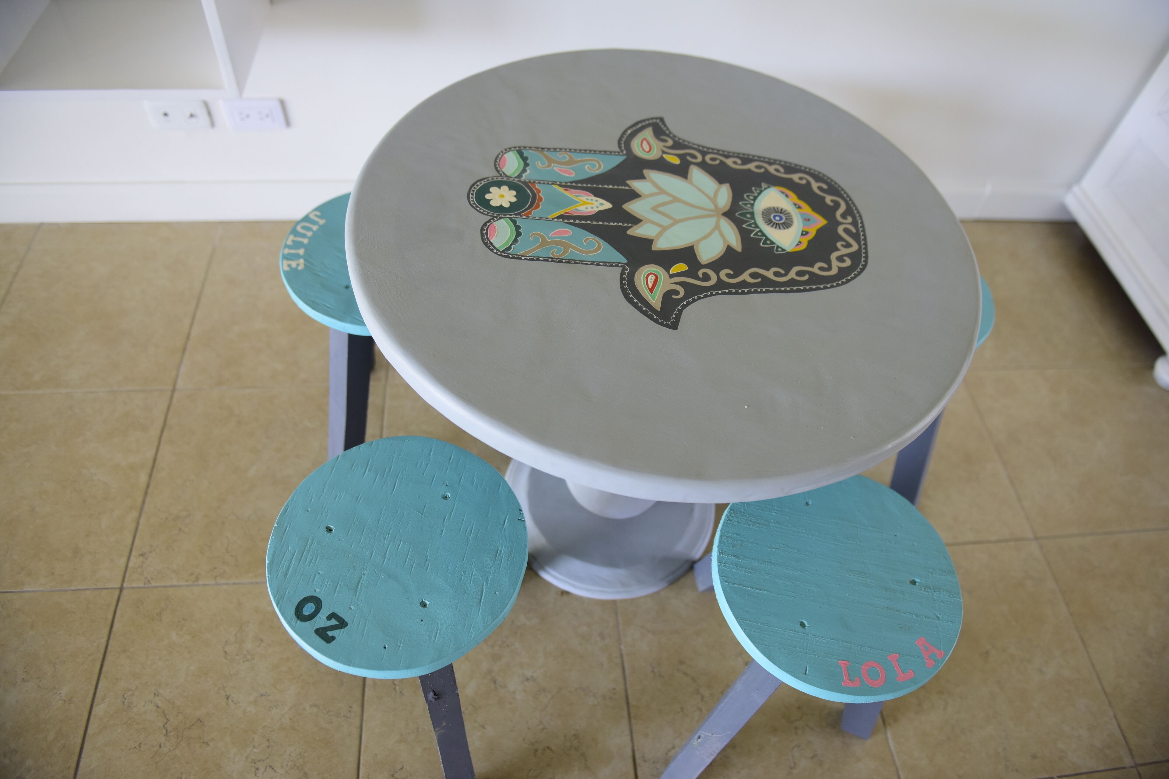 A small round table with a decorative top and four turquoise chairs with numbers on them.