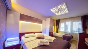 A hotel room with a large bed, bedside tables, a desk, and a window with curtains.