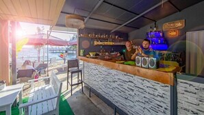 An outdoor bar area with a stone counter, bar stools, and a view of the beach.