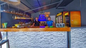 A bar area with shelves of bottles and glasses, a blue neon sign, and a speaker system.