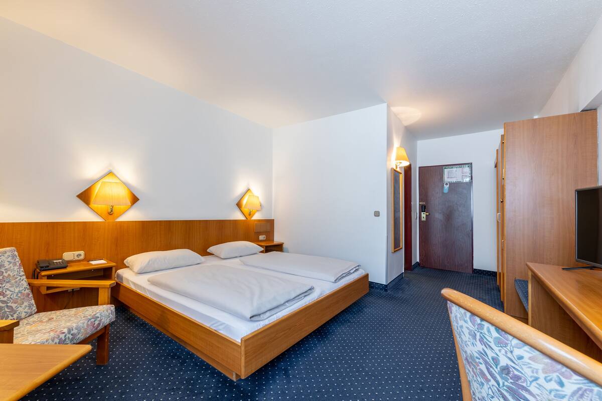 A hotel room with a bed, a desk, a chair, and a television.