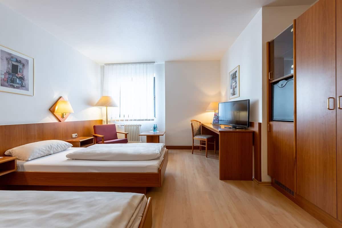 A hotel room with a bed, a desk, a chair, a television, and a wardrobe.