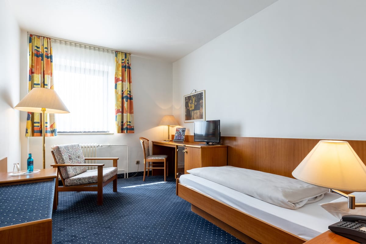 A hotel room with a bed, a desk, a chair, a television, and a window with curtains.